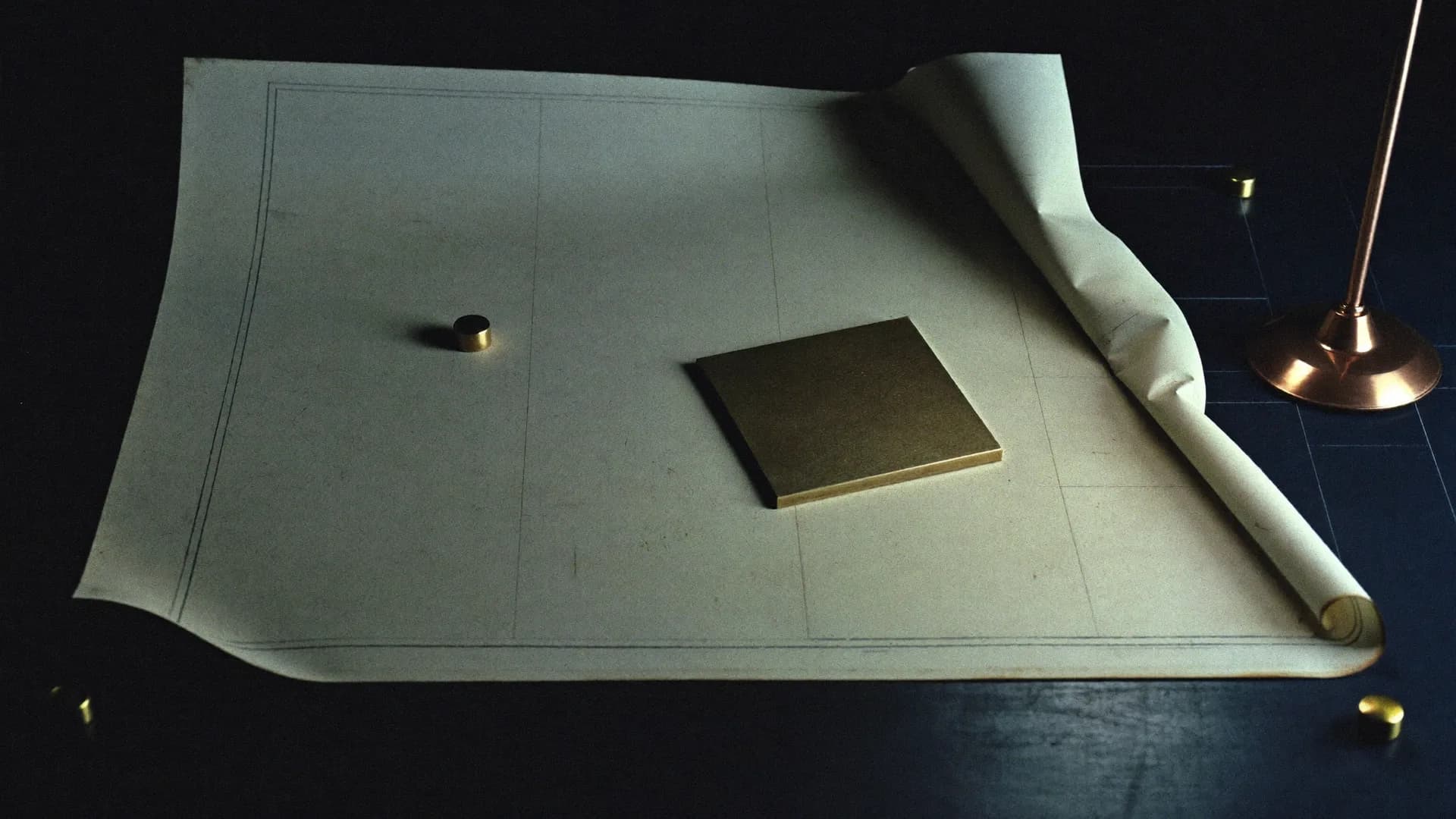 A large unrolled drafting sheet with faint grid lines, held flat by a brass plate and a small brass weight