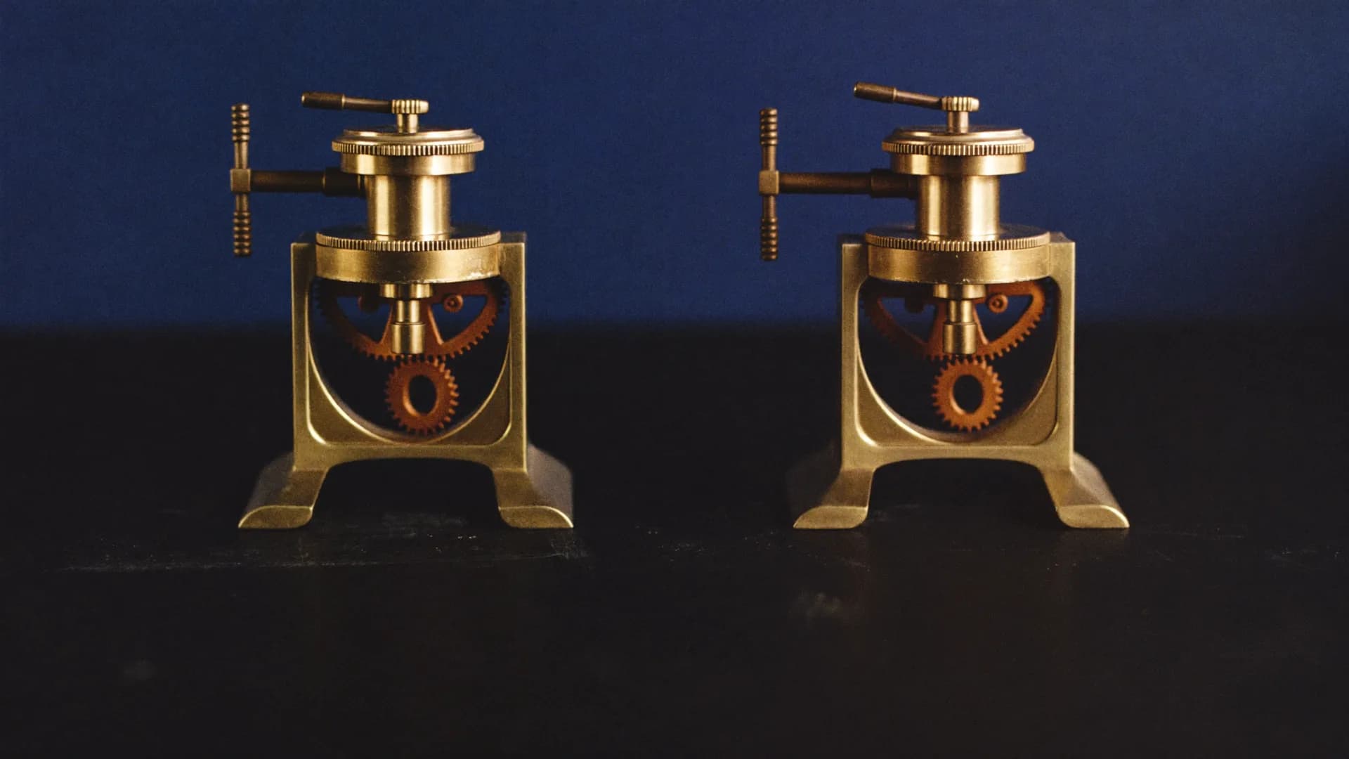Two identical brass mechanisms standing side by side on a dark bench