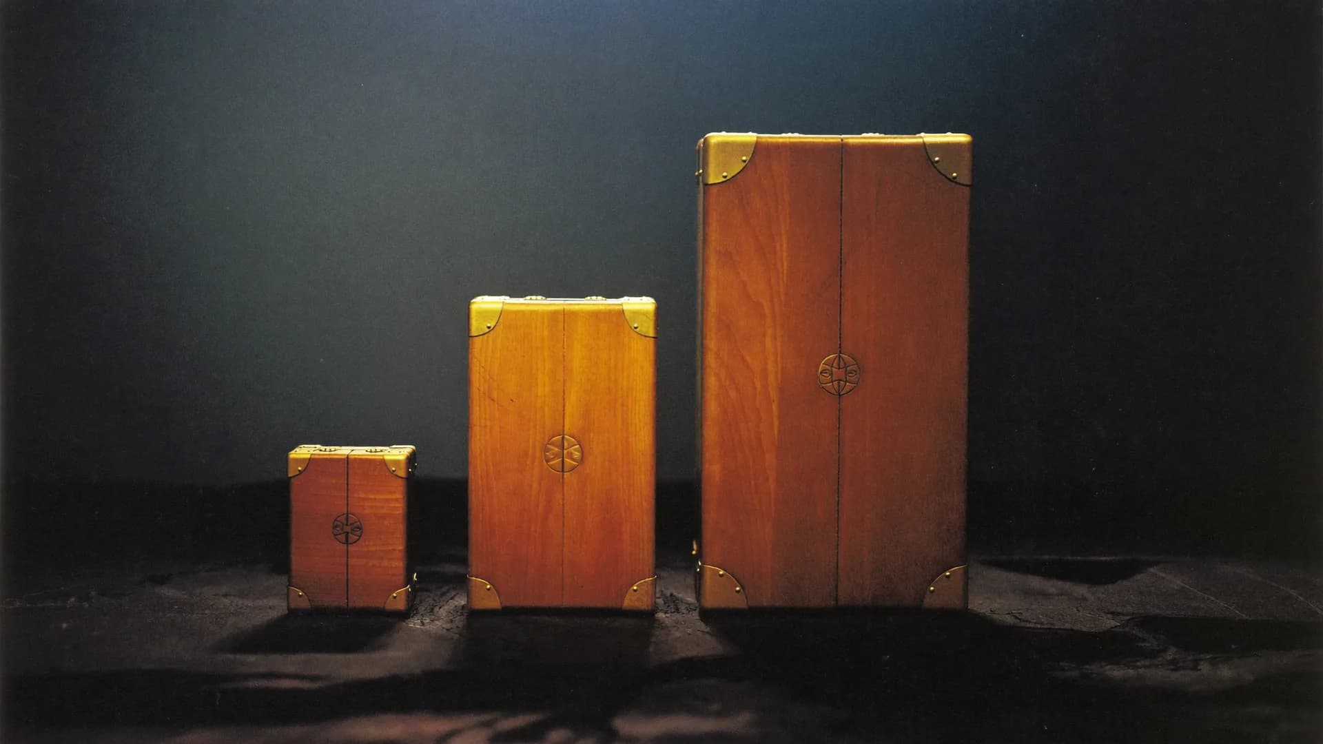 Three brass-cornered cases of increasing size in a row on dark stone