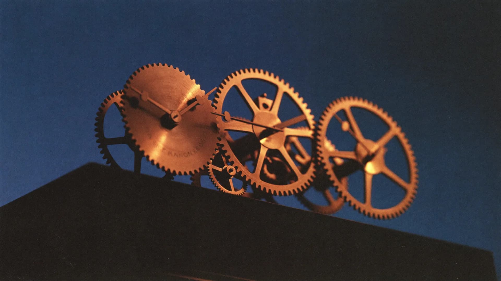 Brass gears meshing on a dark bench under warm copper light