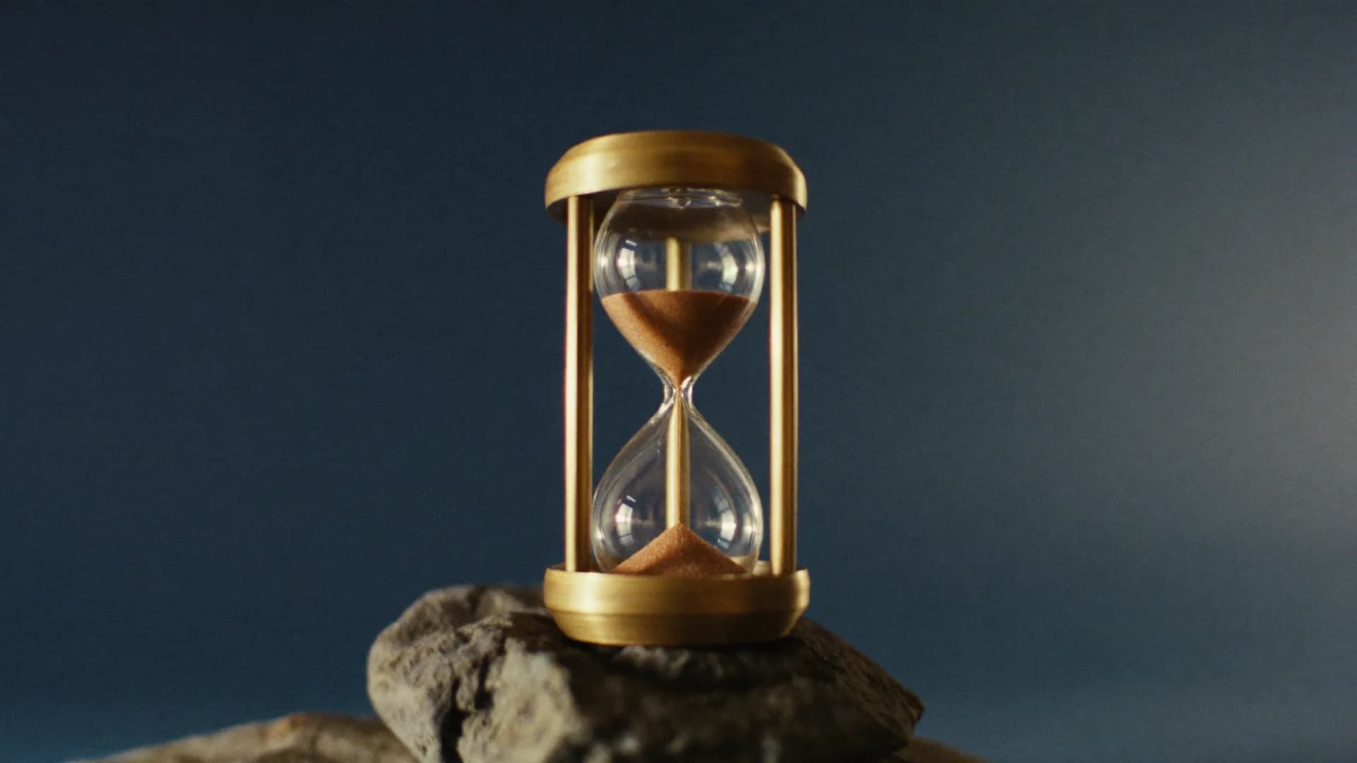 A brass hourglass with copper sand mid-flow on dark stone